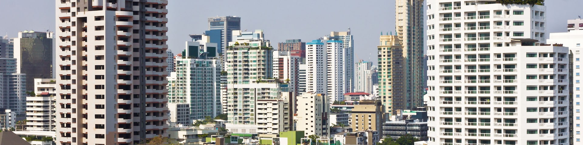 Paisagem urbana com edifícios modernos altos, alguns com varandas e áreas verdes.