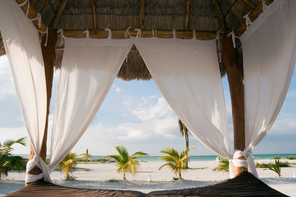 A beach with a thatched roof structure and white drapes.