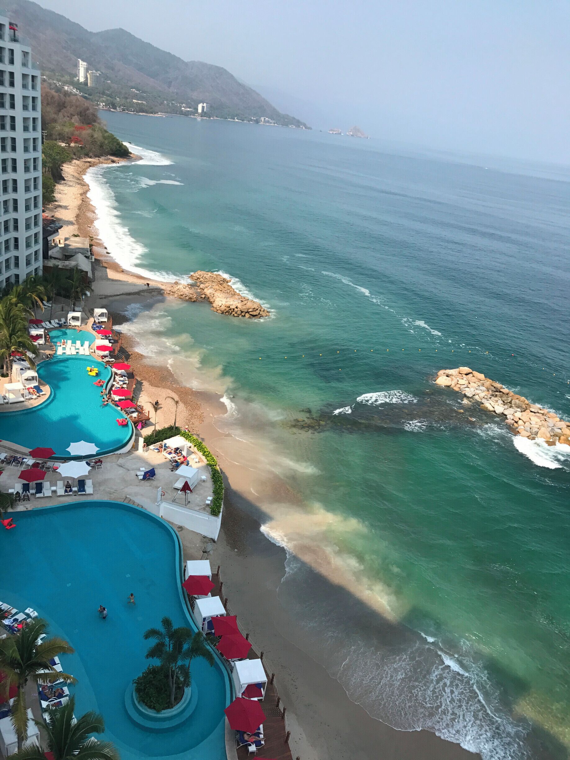 A coastal resort with a swimming pool, beach, and rocky shoreline.