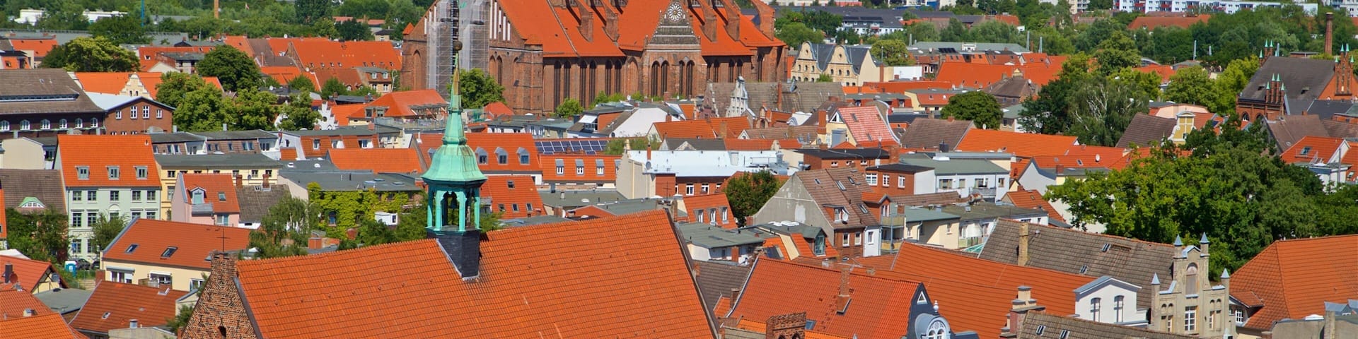 A town with red-tiled roofs, a prominent church with a clock tower, and a green-roofed tower.