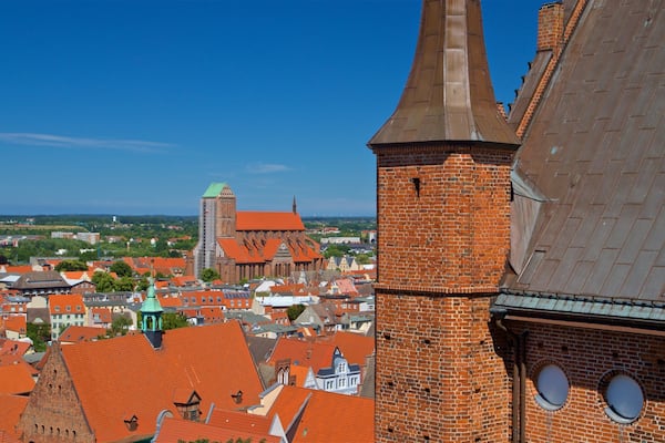 A cityscape with red-roofed buildings, a prominent church with a tall spire, and a brick tower with circular windows.