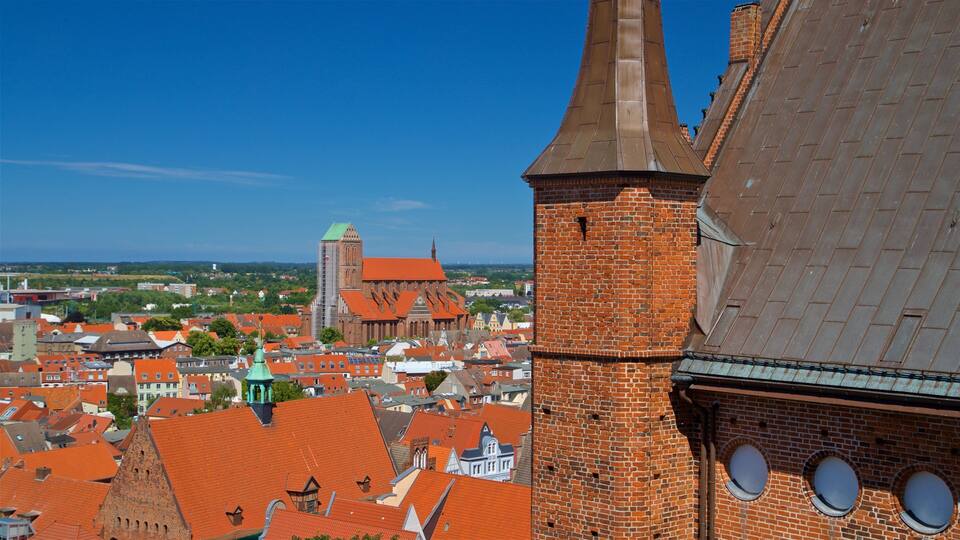Stadsgezicht met rode daken, een opvallende kerk met een hoge torenspits en een bakstenen toren met ronde ramen.