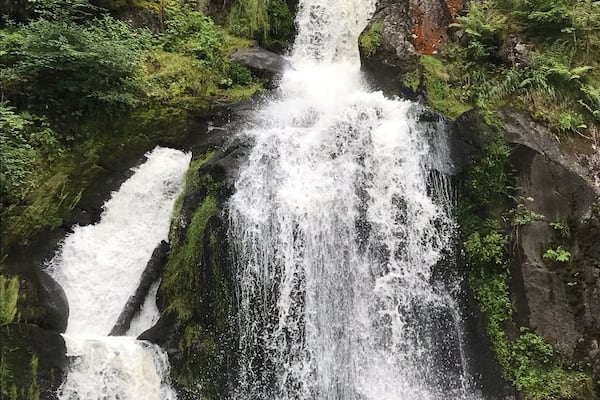 Ein mehrstufiger Wasserfall, umgeben von üppiger Vegetation und moosbewachsenen Felsen.