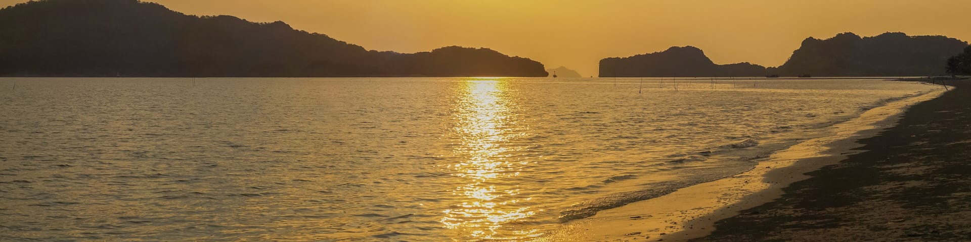 view panorama seaside evening on long beach of limestone mountain in the sea with yellow sun light and cloudy sky background, sunset at Pak Bara Beach, La-ngu District, Satun, southern Thailand.
