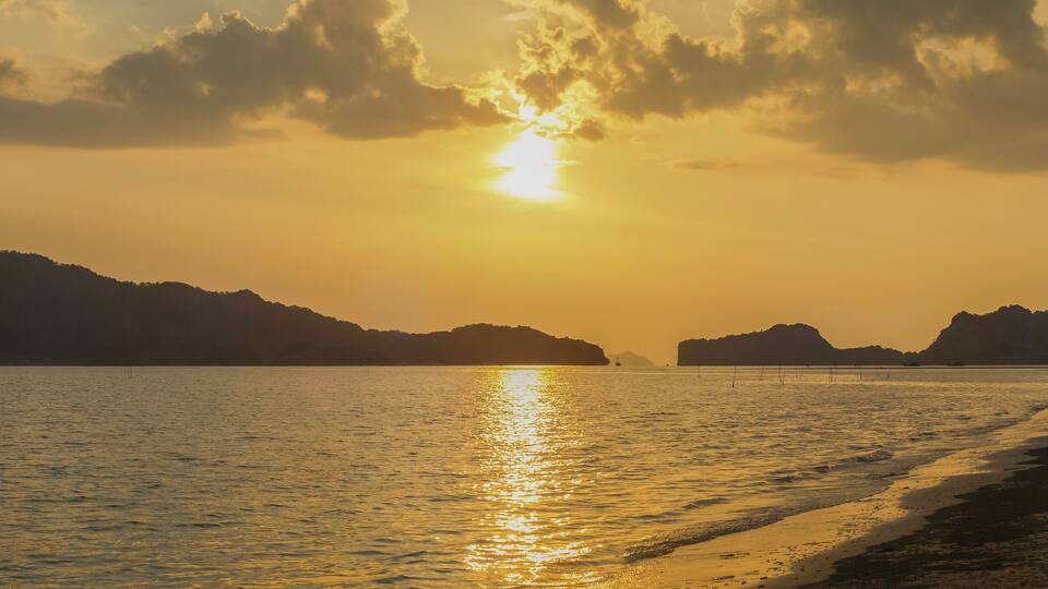 A sunset over a calm sea with a beach and distant mountains.