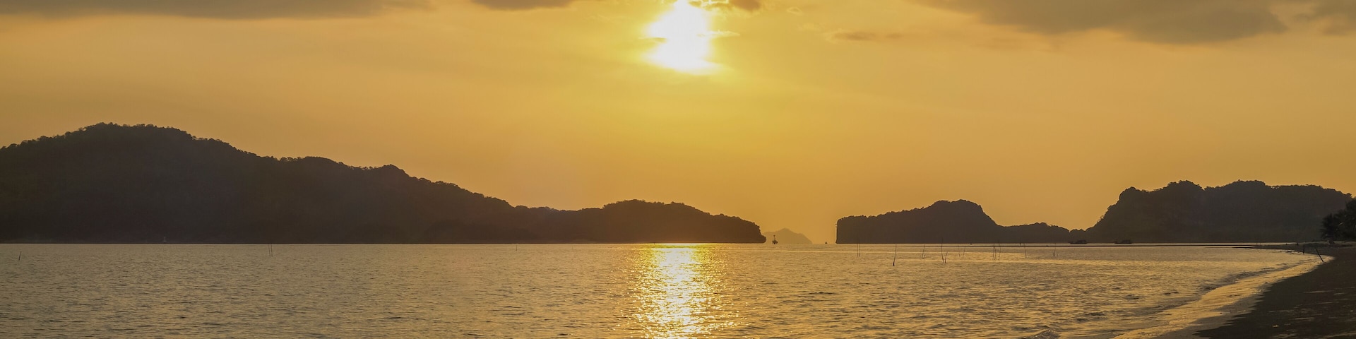 view panorama seaside evening on long beach of limestone mountain in the sea with yellow sun light and cloudy sky background, sunset at Pak Bara Beach, La-ngu District, Satun, southern Thailand.