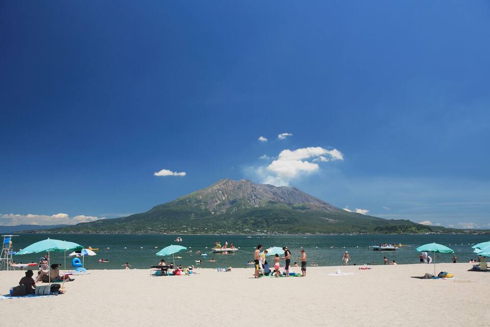 Uma praia com pessoas, guarda-sóis e uma montanha ao fundo.