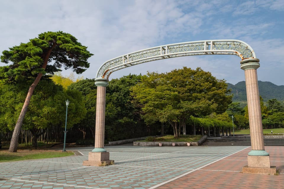 Un parque con un arco decorativo, árboles y un camino pavimentado.