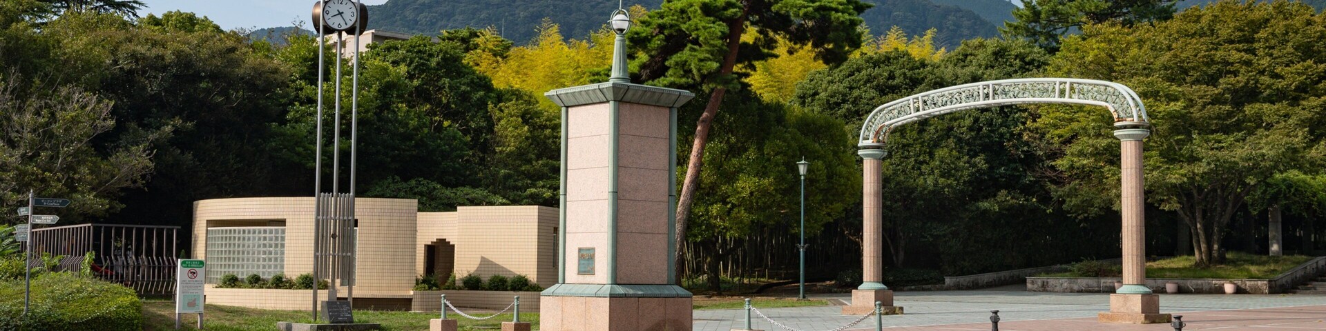 Una entrada al parque con un reloj, un arco de piedra y una montaña al fondo.
