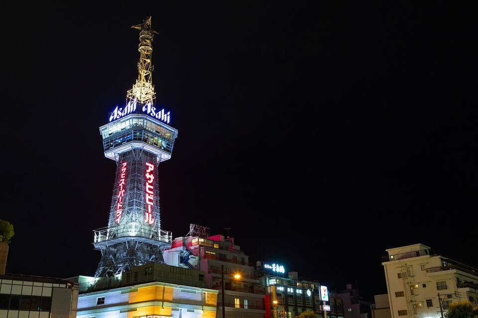 Una torre bien iluminada con señalización luminosa, rodeada de edificios.