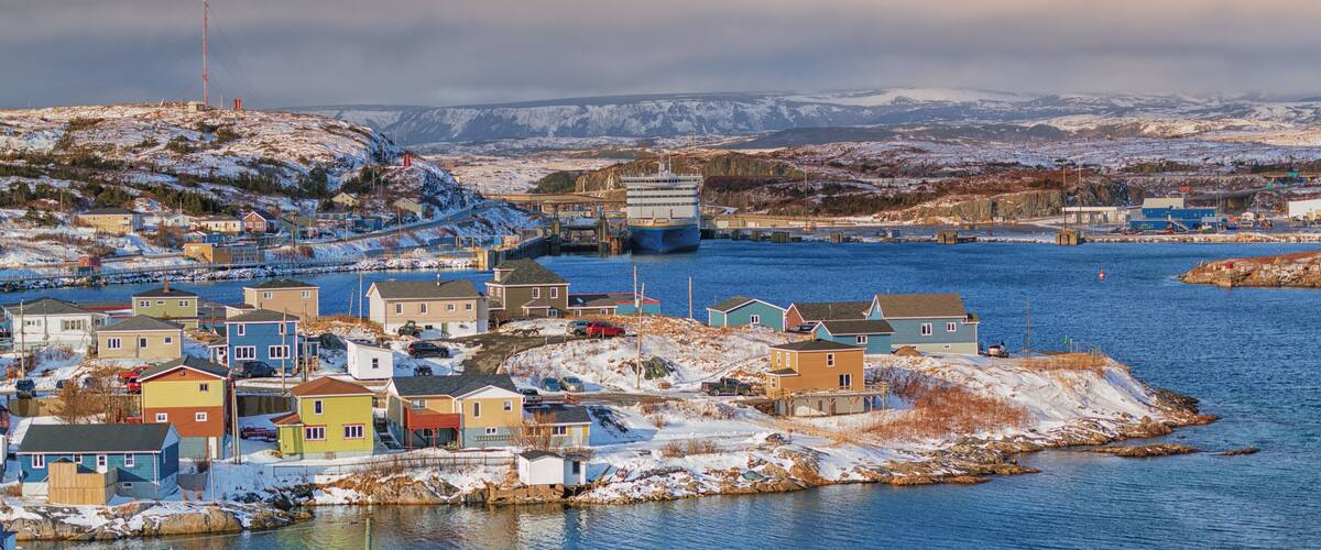A panoramic view of Channel Port aux Basques, Newfoundland during winter. The small coastline community has snow covered colorful houses, Marine Atlantic ferry and terminal with a sheltered harbour.