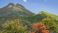 A mountain range with dense forests and autumn-colored trees in the foreground.