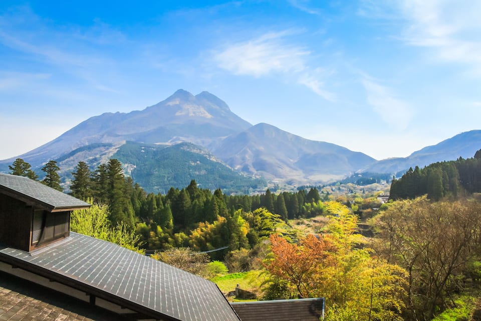 A mountain range with a prominent peak, a valley with autumn-colored trees, and a modern building with a sloped roof.