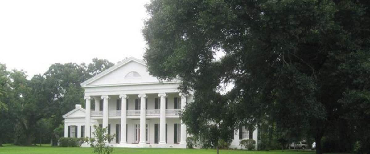 A large white building with columns, surrounded by a grassy field and trees.