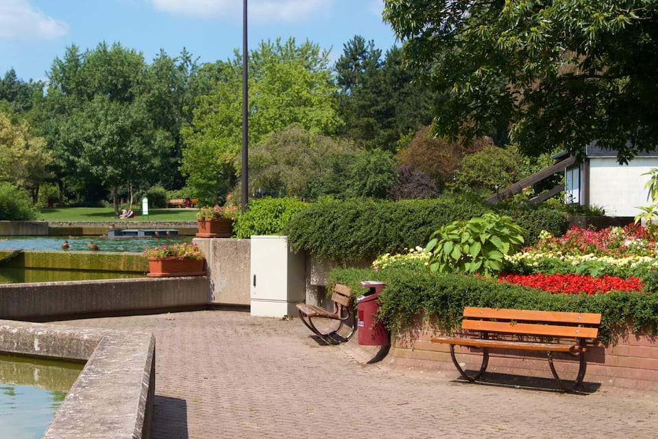 A park with a fountain, a pond, a bench, and a building.
