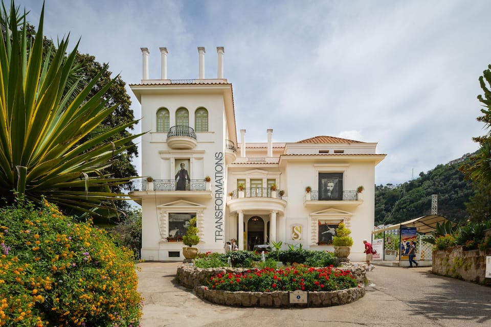 A grand building with a bell tower, surrounded by vibrant flower beds and lush greenery.