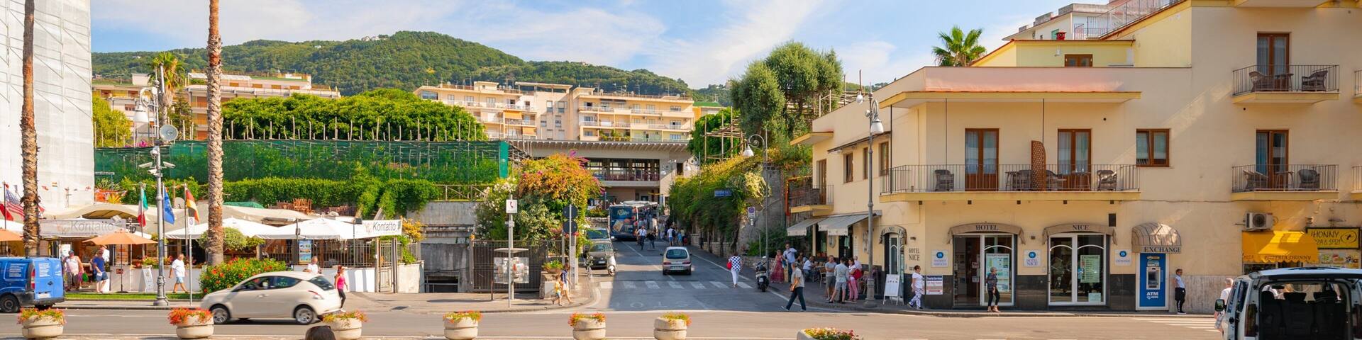 A bustling street with palm trees, a hotel, and a café.