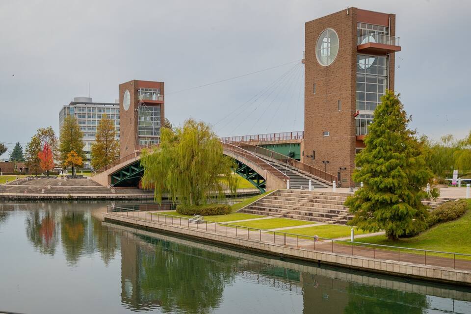 A riverside walkway with a bridge, a clock tower, and a modern building.