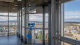 A panoramic view from a high-rise building with large windows, a blue telescope, and a map on the wall.