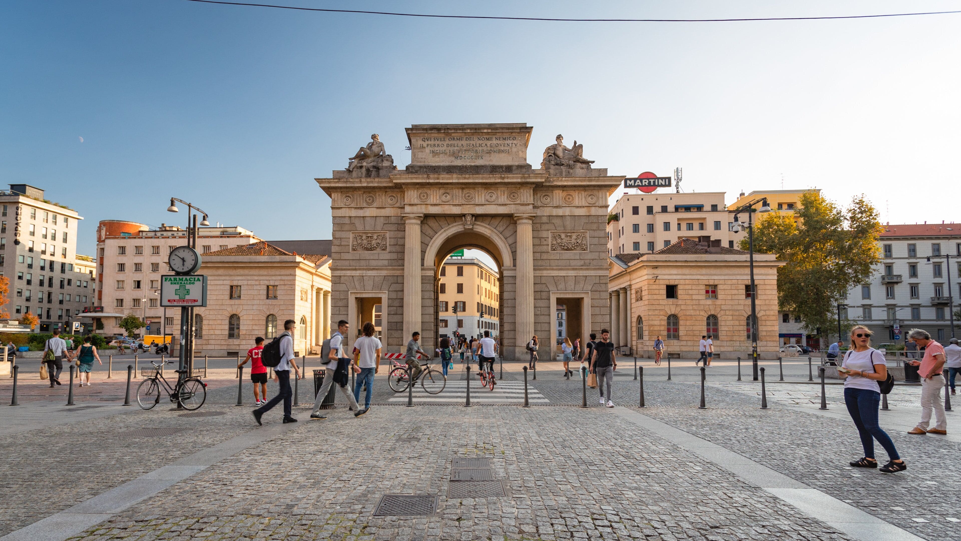 A historic archway with inscriptions, surrounded by cobblestone pavement and modern buildings.