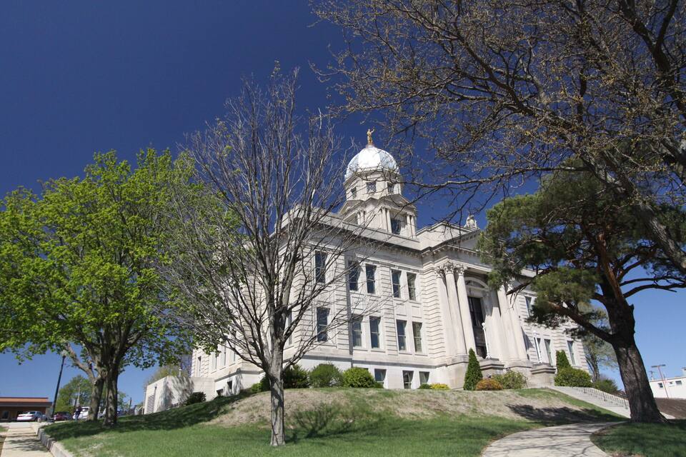 A large, historic building with a dome and columns, surrounded by trees and a grassy area.