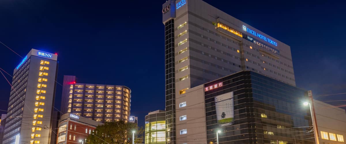 A cityscape at night with illuminated buildings, including the Excel Hotel Tokyo and other commercial structures.