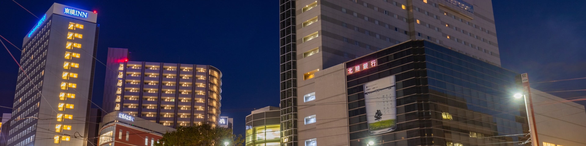 A cityscape at night with illuminated buildings, including the Excel Hotel Tokyo and other commercial structures.