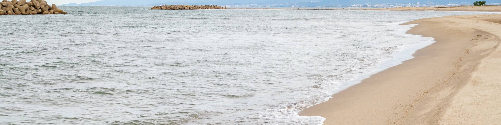 A sandy beach with gentle waves and a rocky outcrop in the distance.