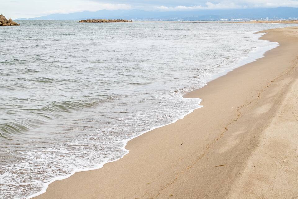 A sandy beach with gentle waves and a rocky outcrop in the distance.