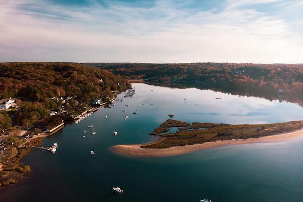 Cold Spring Harbor, New York with sandbar, woods, and various boats in the water.