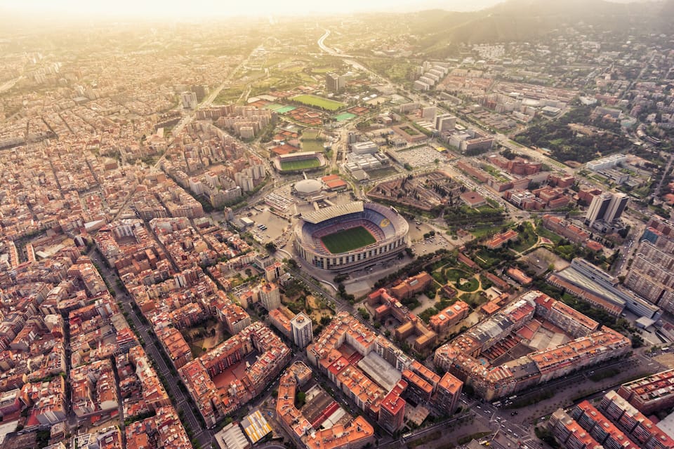 An aerial view of a city with a large stadium surrounded by dense urban buildings and green spaces.