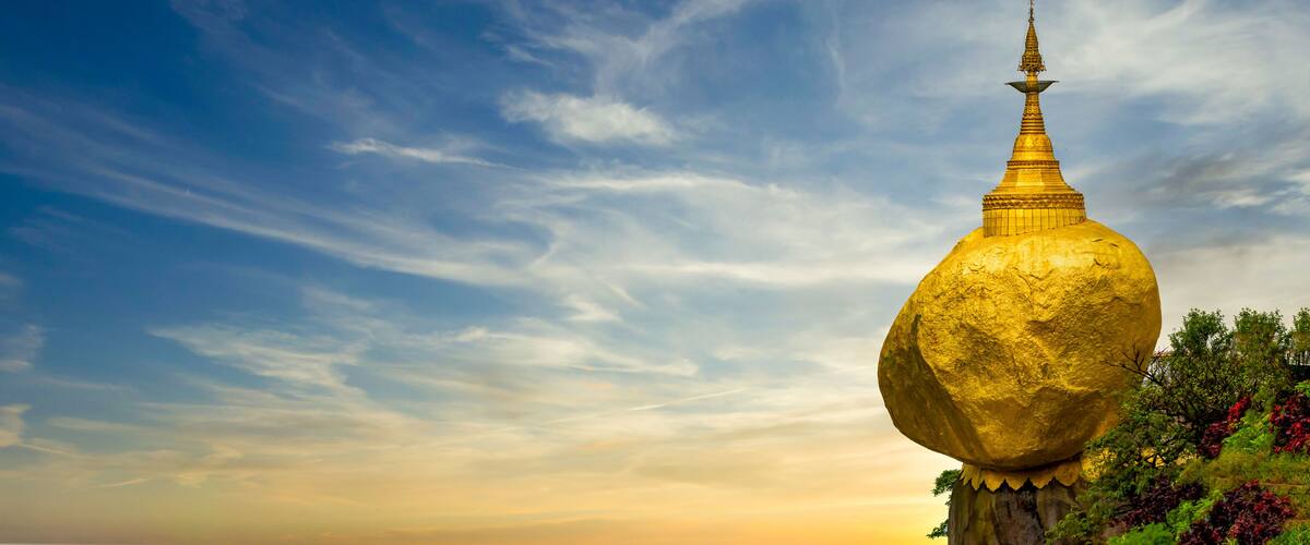 A golden stupa with a spire, set against a sky with wispy clouds.