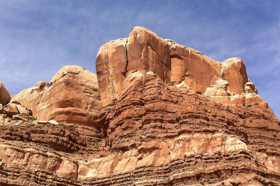A large rock formation with layered strata and a clear blue sky.