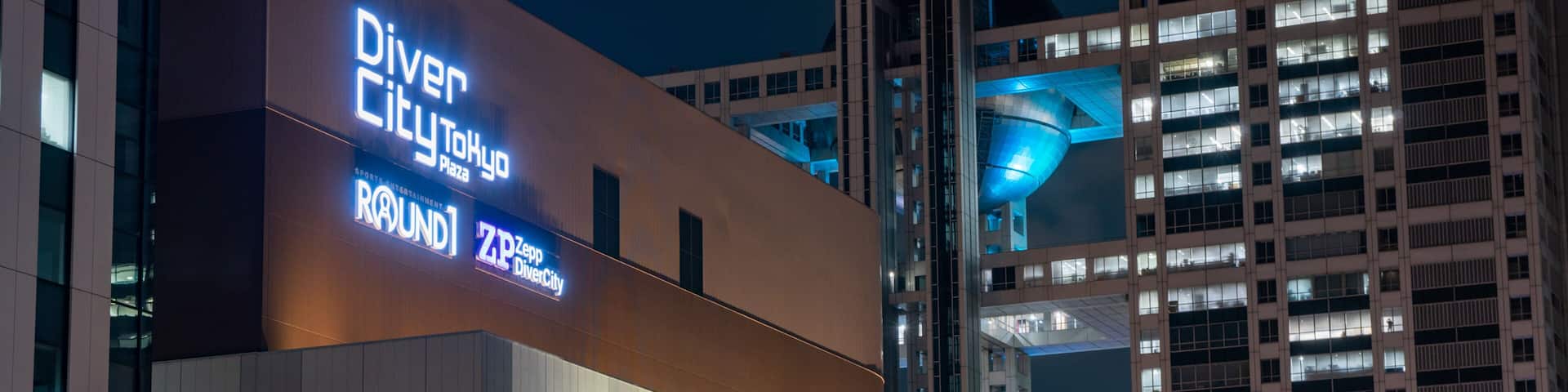 A modern building with illuminated signs for Zara, GUCCI, H&M, ABC-MART, and Skechers.
