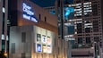 Un bâtiment moderne avec des enseignes lumineuses pour Zara, Gucci, H&M, ABC-MART et Skechers.