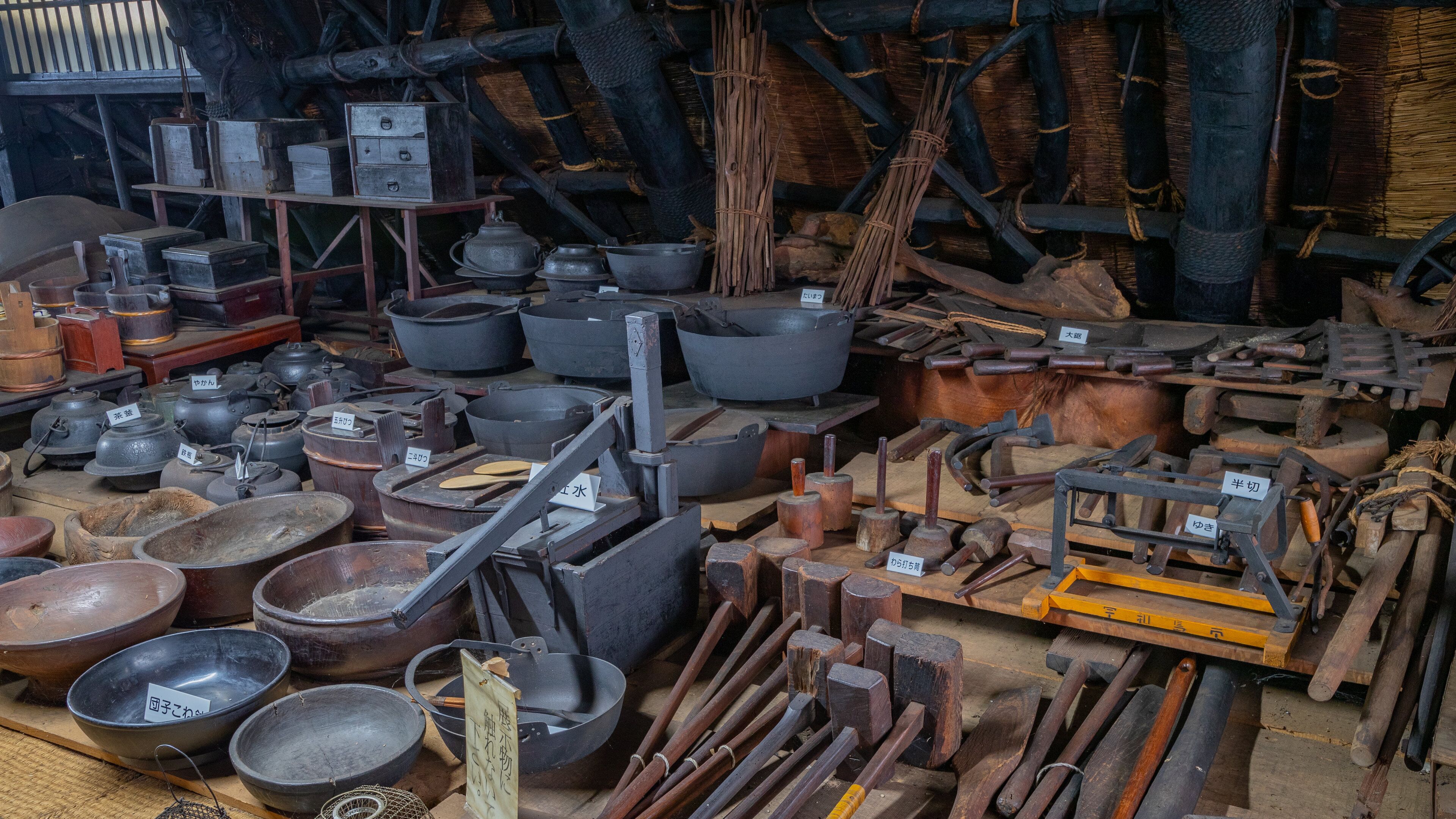 A variety of traditional cooking utensils and tools, including pots, pans, and wooden implements, displayed in an indoor setting.