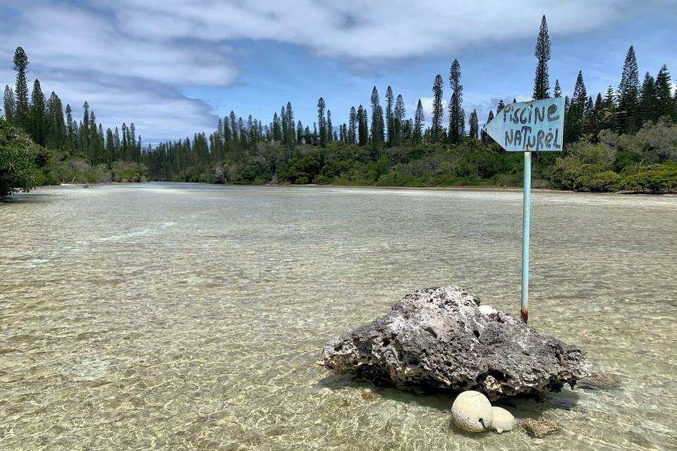 A clear lake with a sign reading "PRESERVE NATURAL" and a large rock in the water.