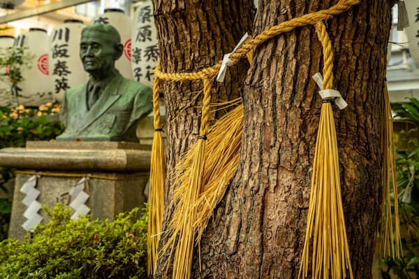Un arbre décoré de cordes en macramé, avec une statue en arrière-plan.