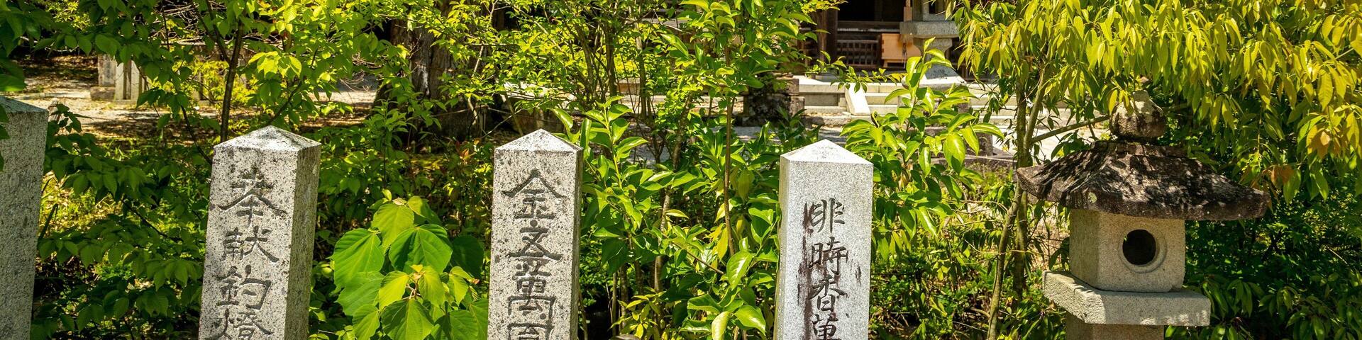 A traditional Japanese temple surrounded by lush greenery and stone markers.