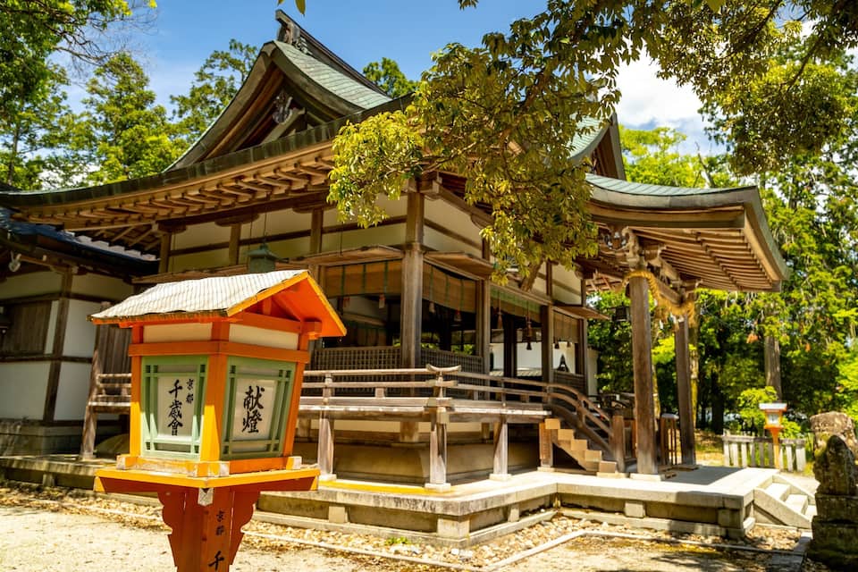 Een traditionele Japanse tempel met een houten constructie, een stenen lantaarn en een stenen standbeeld op de voorgrond.