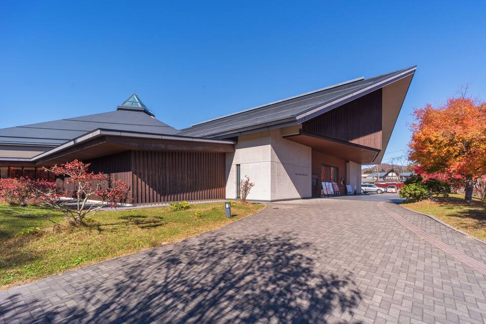 A modern building with a unique roof design, surrounded by a well-maintained garden with autumn-colored trees.