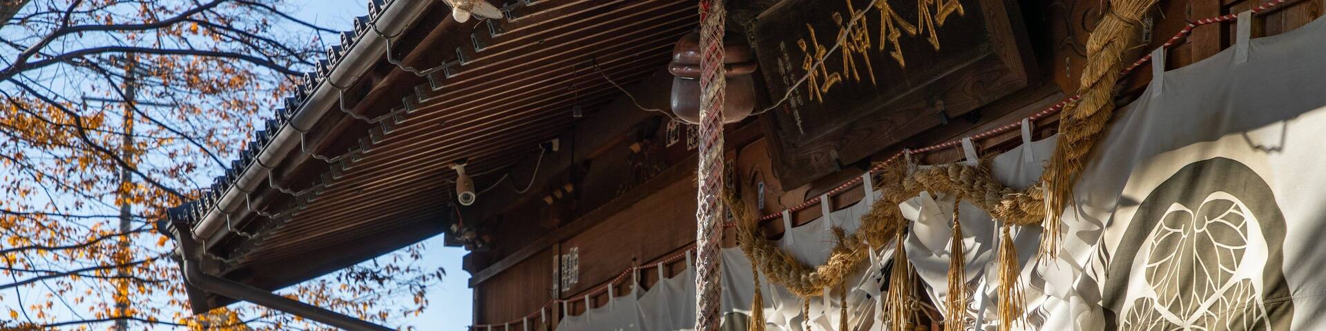 A traditional Japanese building with wooden architecture, a hanging decorative rope, and a white banner with a circular design.