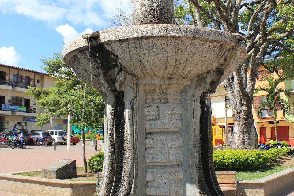 A stone fountain with a decorative top and curved legs in a public square.