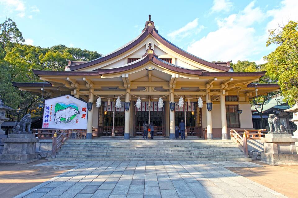 A traditional Japanese temple with a curved roof, stone steps leading up to the entrance, and statues of lions on either side.