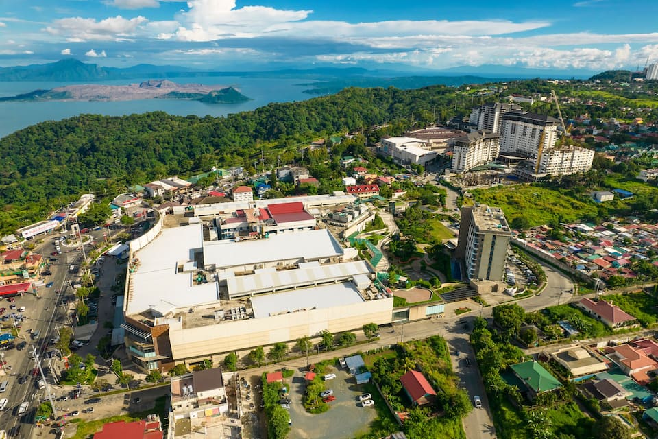 Vista aérea de uma cidade costeira, com um grande edifício industrial, áreas residenciais e um cenário montanhoso.