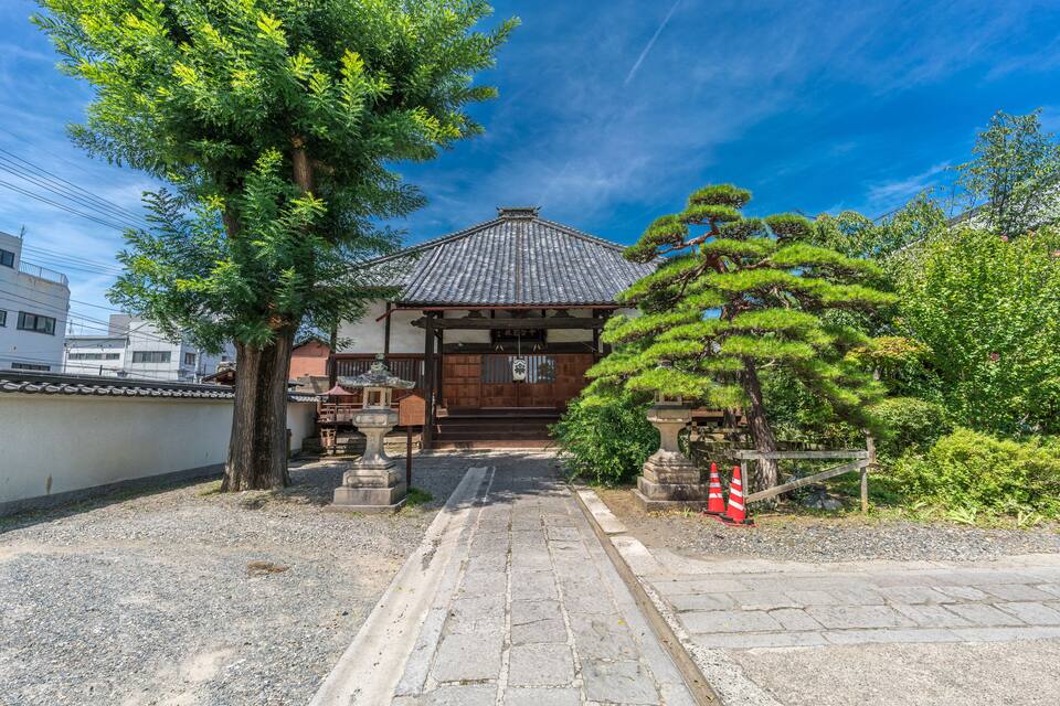A traditional Japanese building with a tiled roof, surrounded by trees and gravel paths.