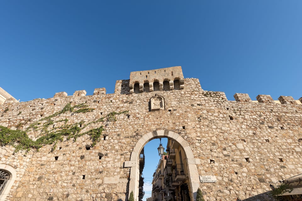 A historic stone wall with an arched entrance and a clock tower.