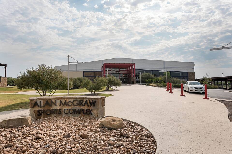 The exterior of the Alan McGraw Sports Complex with a clear sky and a sign in front.