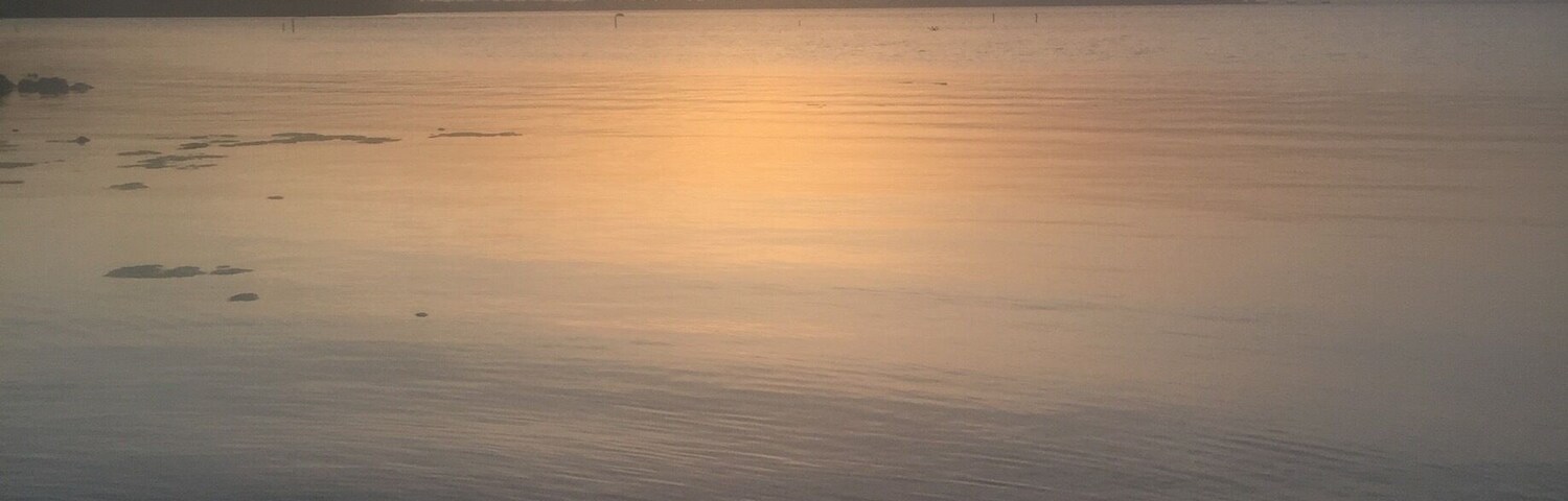 Água calma refletindo um pôr do sol.
