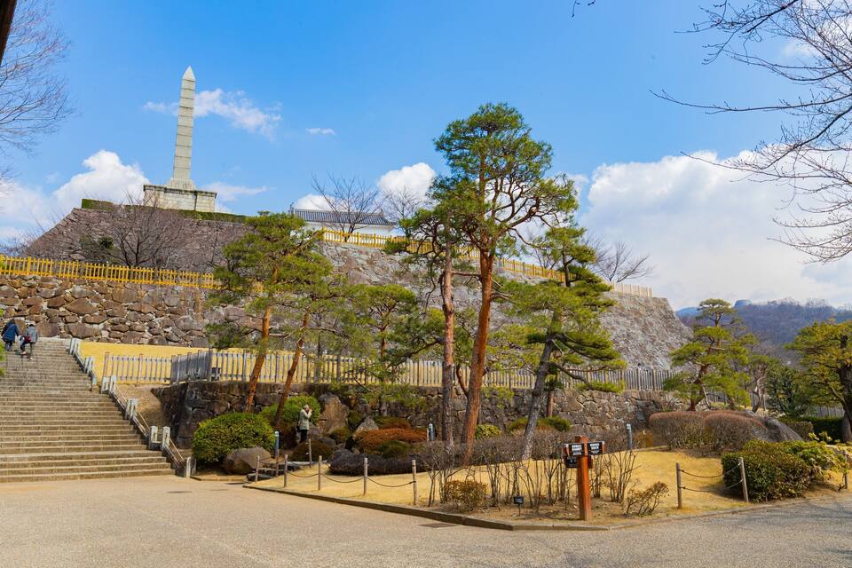 A stone monument, a stone staircase, and a forested hill.